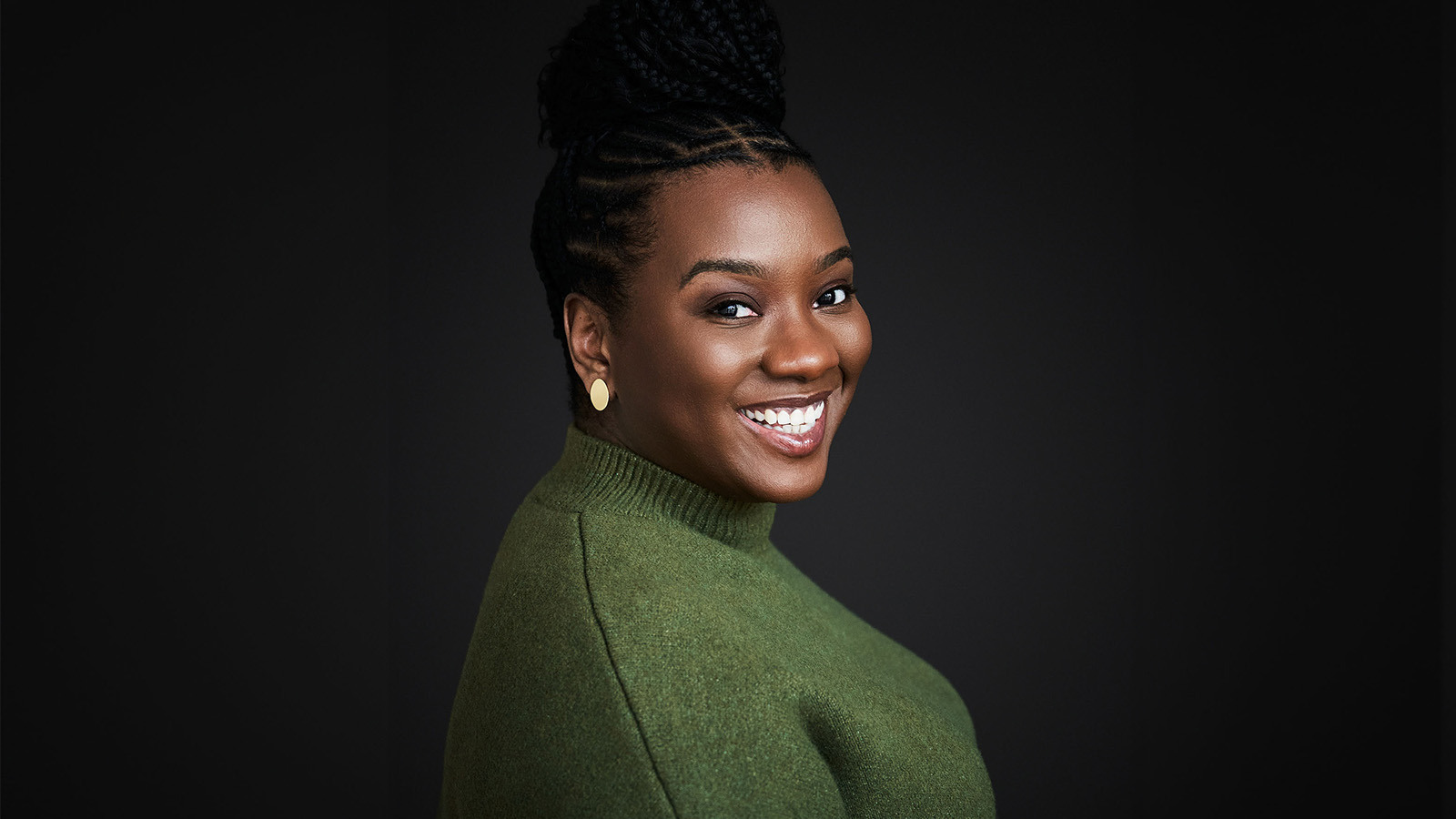 CeCe Taylor smiles at the camera. Her hair is up in a braided bun and she’s wearing a green sweater and gold earrings.