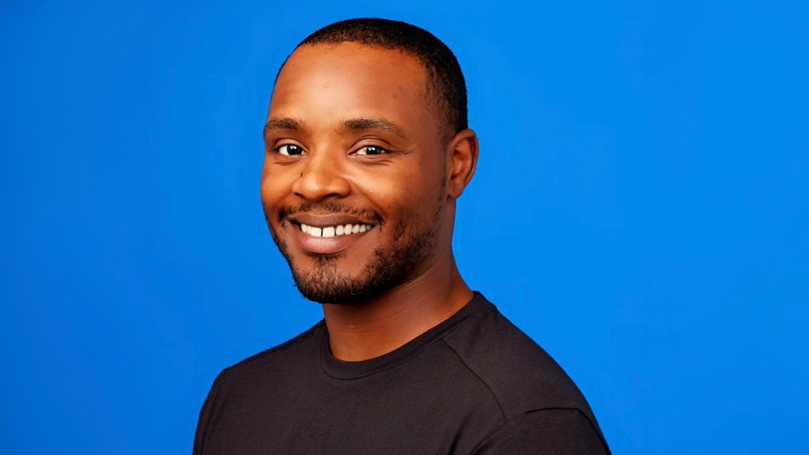 Lamont Johnson smiles at the camera in front of a blue background. He is wearing a black shirt.