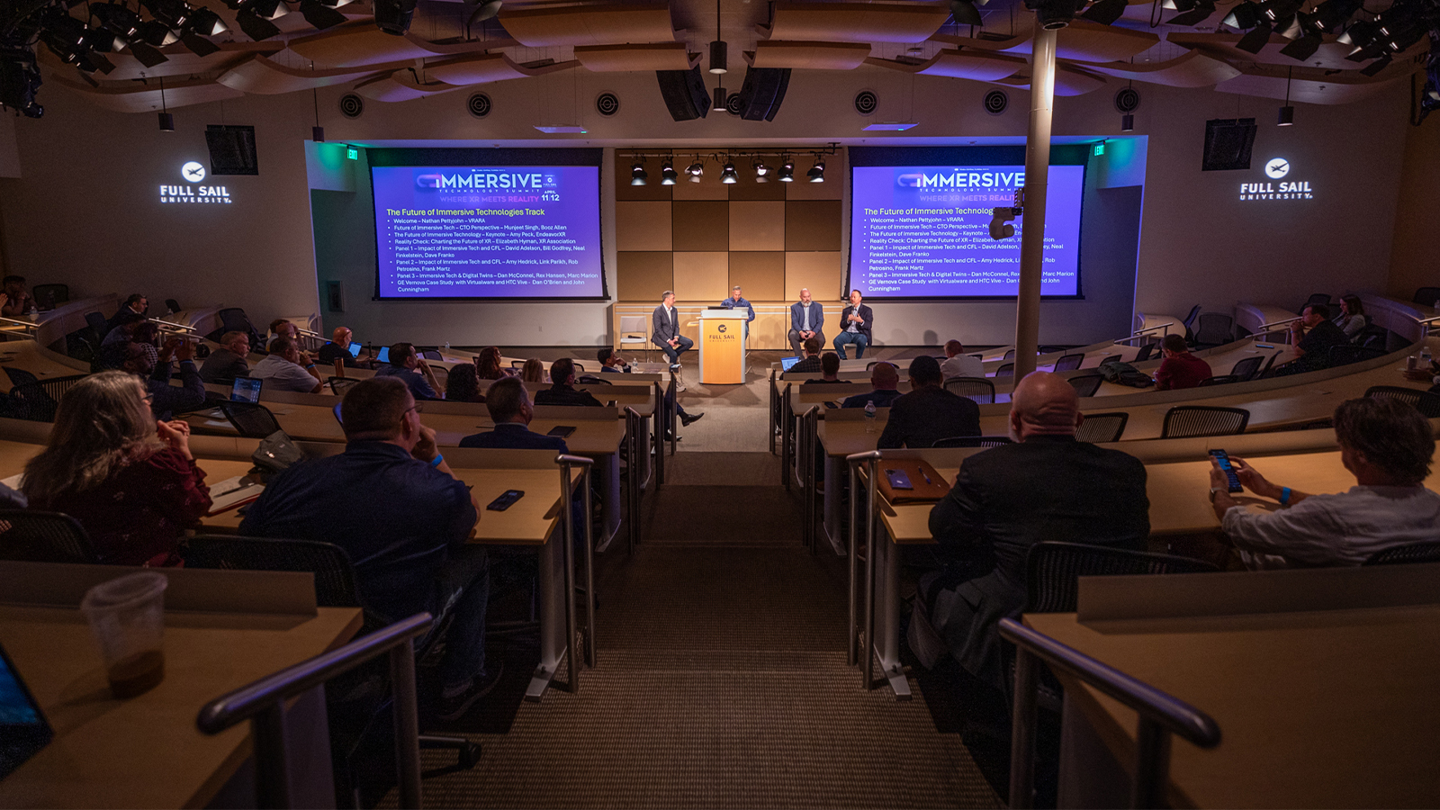 An audience watches a group of panelists give a presentation on stage at Central Florida's Second Annual Immersive Technology Summit.