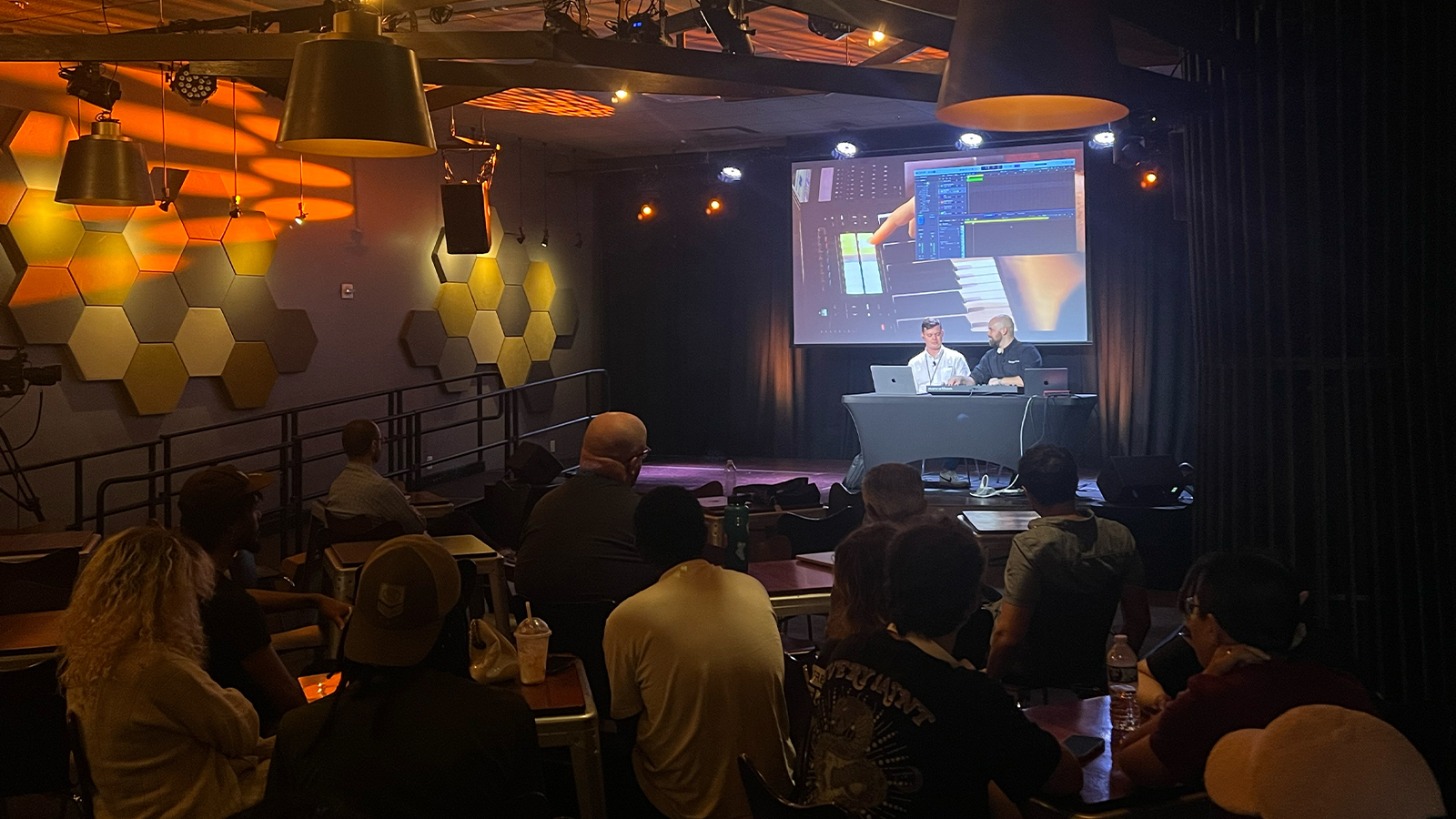 Scott Dickinson and Evan Weiss sit onstage with a keyboard and two laptops. Students sit in an audience facing the stage.
