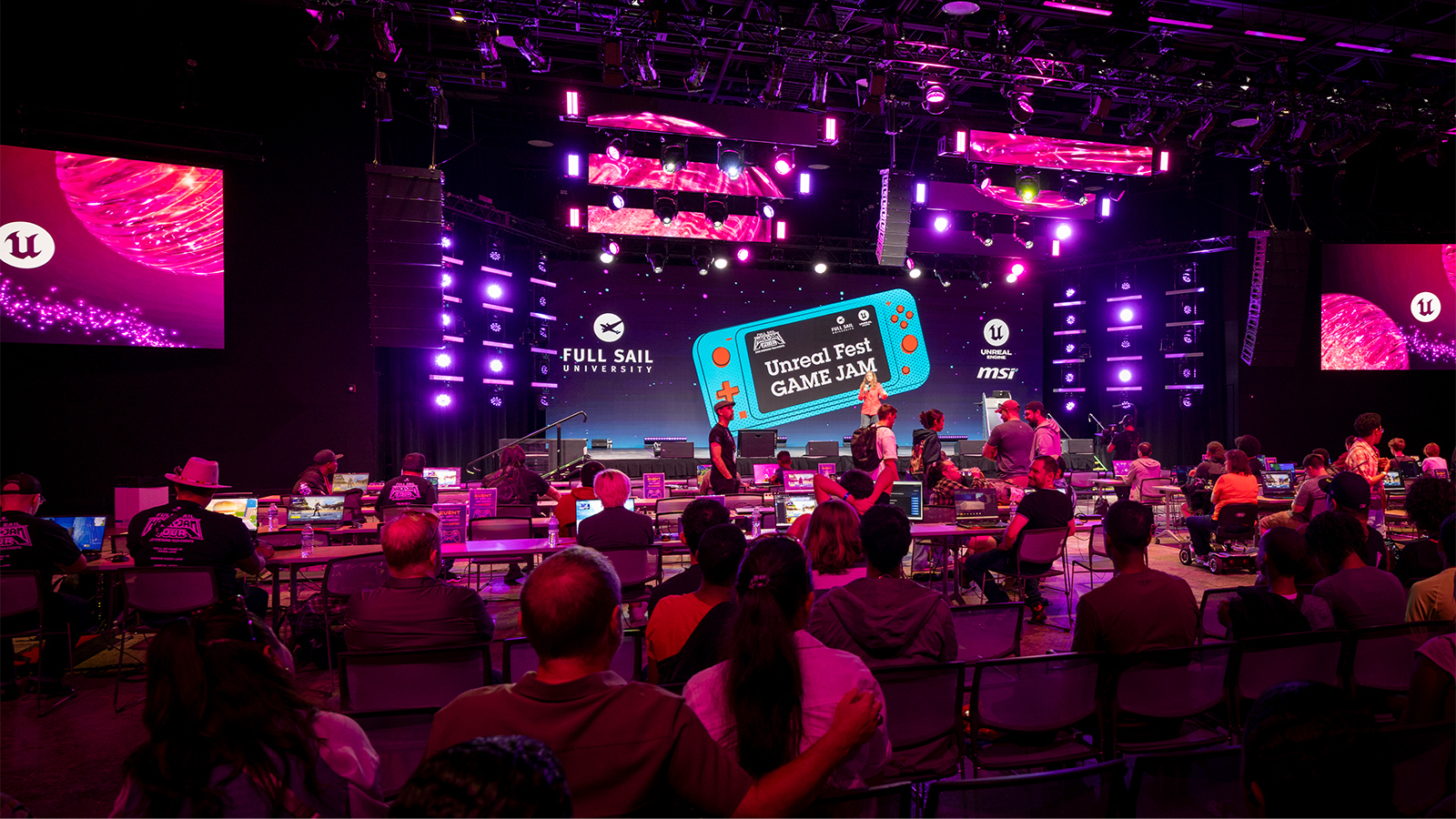 Full Sail Live, lit in a purple hue, is filled with a crowd seated at workstations during the Unreal Fest Game Jam.