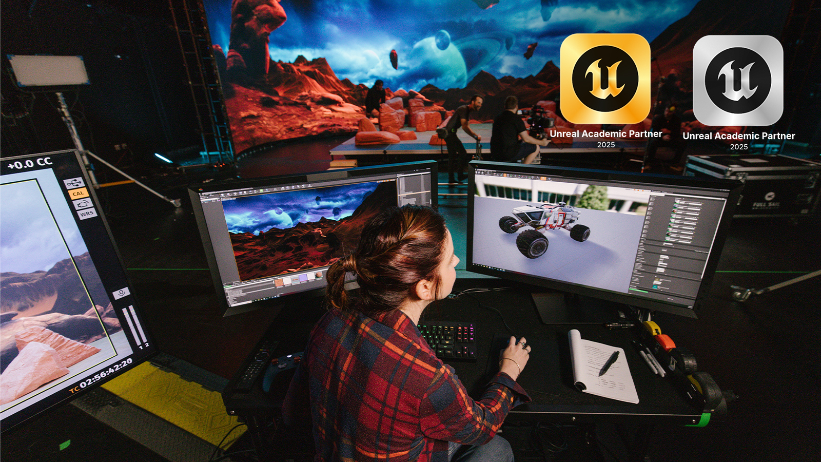 A student creates a space rover vehicle in Unreal Engine on a computer in Full Sail’s virtual production studio. A virtual background with a desert planet is on an LED wall in front of them.