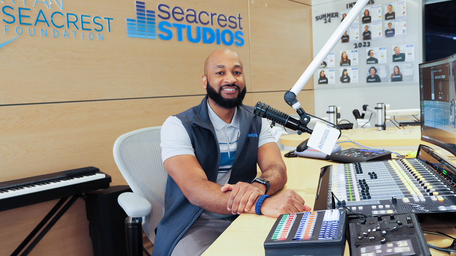 Full Sail grad Anthony Grier sits in front of an audio board at Orlando Health Arnold Palmer Hospital for Children’s Seacrest Studios, smiling.
