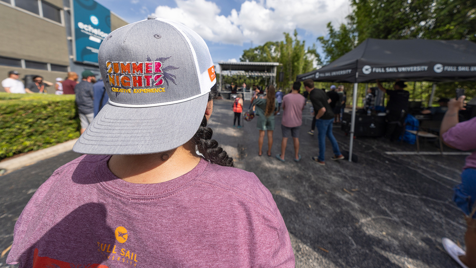 An attendee wearing Summer Nights merch looks toward a Full Sail outdoor stage, surrounded by tents and a lively crowd.