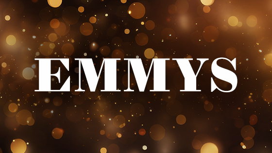 The word 'EMMYS' appears in block white text over a dark, blurred scene filled with warm, glowing lights in shades of gold, orange, and brown.