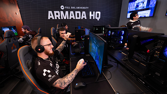 Gamers compete at Full Sail’s Armada HQ, celebrating a win in a high-energy esports match surrounded by teammates and gaming stations.