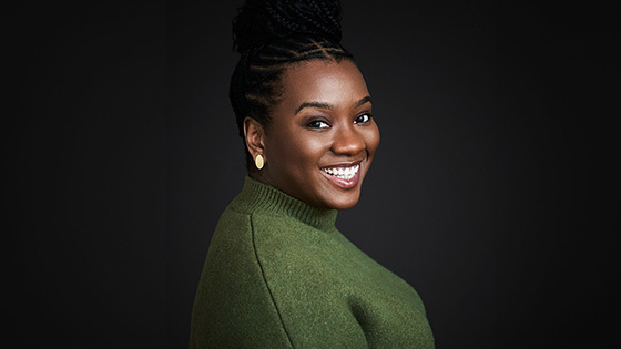 CeCe Taylor smiles at the camera. Her hair is up in a braided bun and she’s wearing a green sweater and gold earrings.