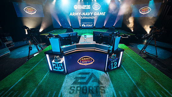 A green-turf stage set inside the Full Sail University Orlando Health Fortress for the Army–Navy ‘College Football 26’ esports tournament.
