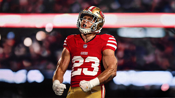 A football player in a red San Francisco 49ers jersey, number 23, celebrating passionately on the field with clenched fists.