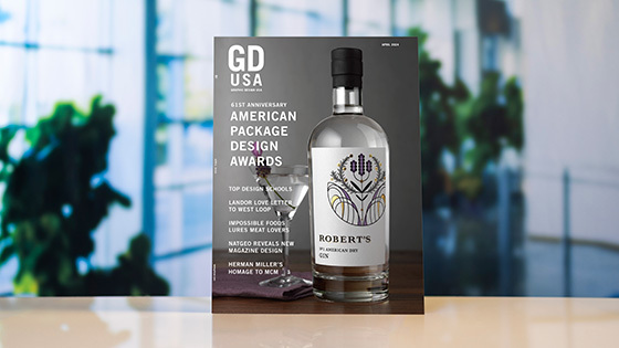 A copy of 'Graphic Design USA' magazine sits atop a white surface against a blurred background. The magazine cover depicts a bottle of gin and a martini glass against a gray background and reads '61st Anniversary American Package Design Awards.