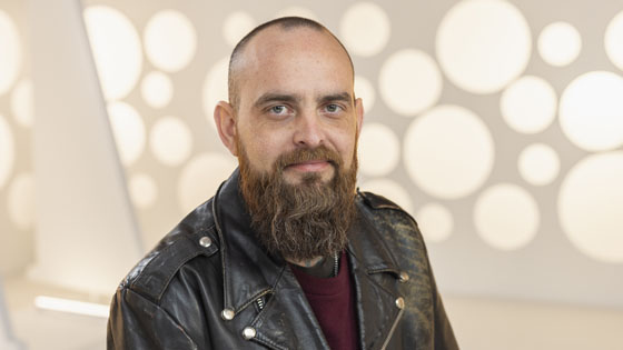 Full Sail Hall of Fame inductee Ben Rice smiles at the camera. He is wearing a burgundy sweater and a black leather jacket.