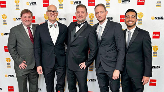Culley Bunker stands with four special effects artists from Skulley FX in front of a VES Awards backdrop. They are wearing suits and smiling.