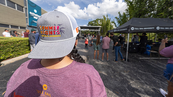 An attendee wearing Summer Nights merch looks toward a Full Sail outdoor stage, surrounded by tents and a lively crowd.