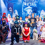 A group of staff members pose for the camera dressed in Halloween costumes including Glinda and Elphaba, the Mandalorian, Loonette the Clown, and more.