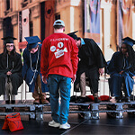 A Coca-Cola Refreshing Films crew member faces seated graduates in caps and gowns during a staged production scene.