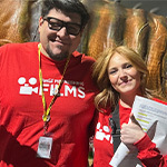 Director Angel and Producer Kylie smile in front of a large animatronic dinosaur tail on set during their film shoot.