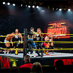 Wrestlers duke it out in the ring during a TNA Impact wrestling match, surrounded by bright stage lights and a cheering crowd in Full Sail's Live Venue.