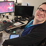 Brock Davis sits at his desk at Blizzard Entertainment. Two computer screens displaying the ‘Diablo IV’ logo are on the desk in front of him.