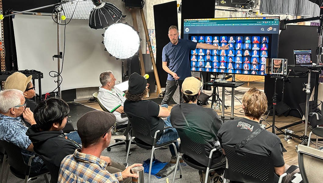 Shawn Rinehart points to a screen displaying headshots of various people and speaks to an audience of students.