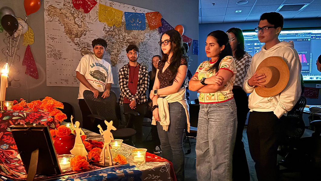 Several students stand in front of a table decorated with candles and flowers. There are balloons and colorful banners on the wall behind them.