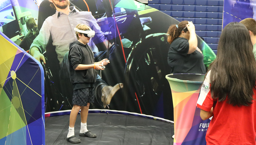 A boy wearing a VR headset interacts with a virtual environment, surrounded by vibrant tech-themed displays and attendees nearby.