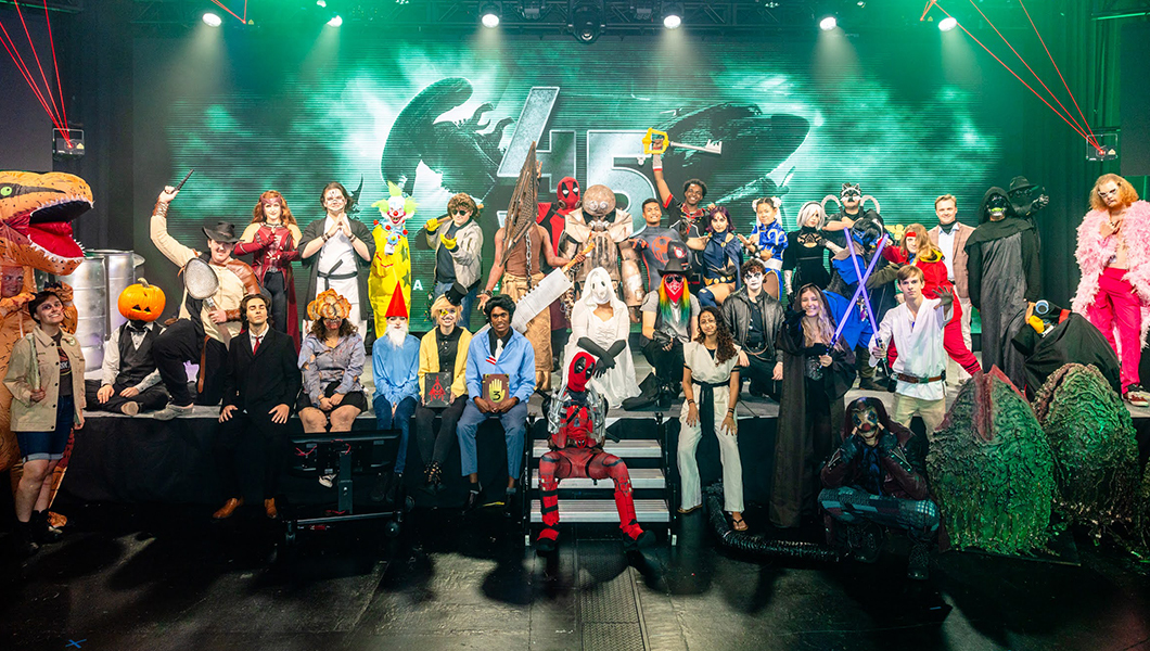 A large group of costumed students poses on stage during Full Sail’s Halloween event as a variety of pop culture characters.