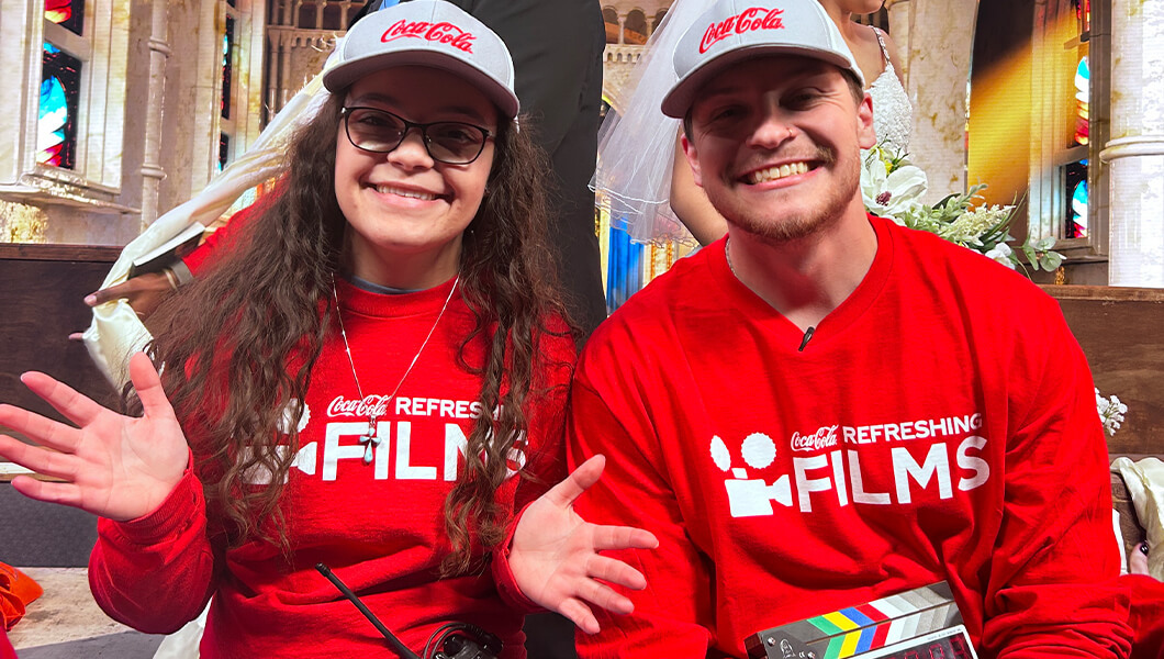 Director Brandon and Producer Christina smile while sitting on a church set holding a clapperboard.