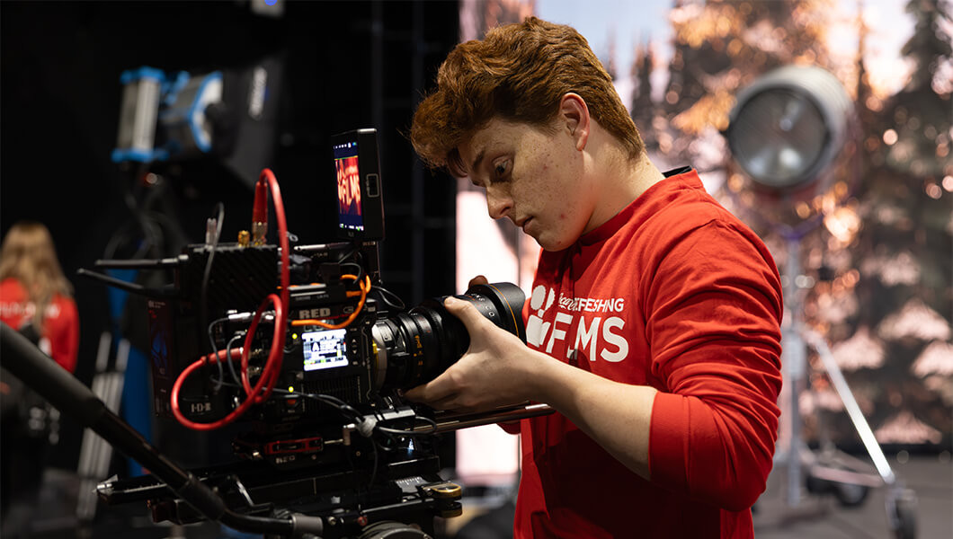 A camera operator in a Coca-Cola Refreshing Films shirt adjusts a RED digital camera on a professional studio set.