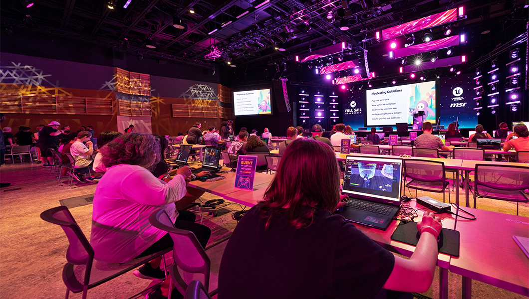 A large venue with rows of workstations featuring gaming laptops and students seated while developing games.