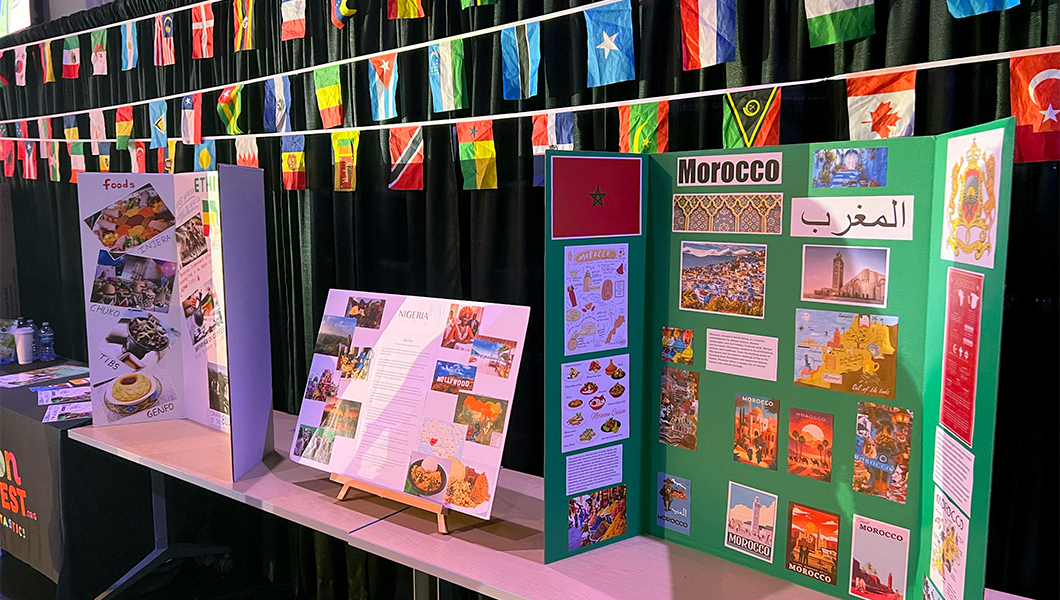 A crowd of students faces a stage where a performer dances with a large screen behind them displaying “Multicultural Festival.” Orange lights shine as the audience claps and cheers.