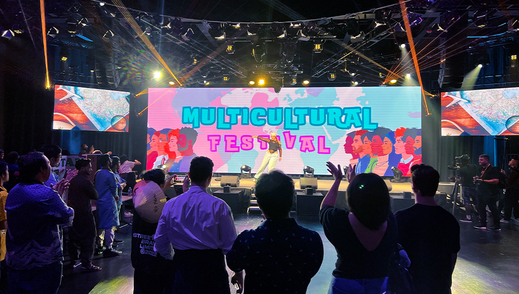 A long table displays three cardboard presentations, one on Ethiopia, one on Nigeria, and one on Morocco. Behind the presentations are black curtains and banners of various countries’ flags.