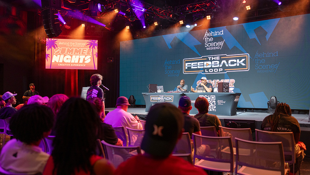 Guests attend a live panel during Full Sail’s Summer Nights event, featuring “The Feedback Loop” on stage under vibrant lights.