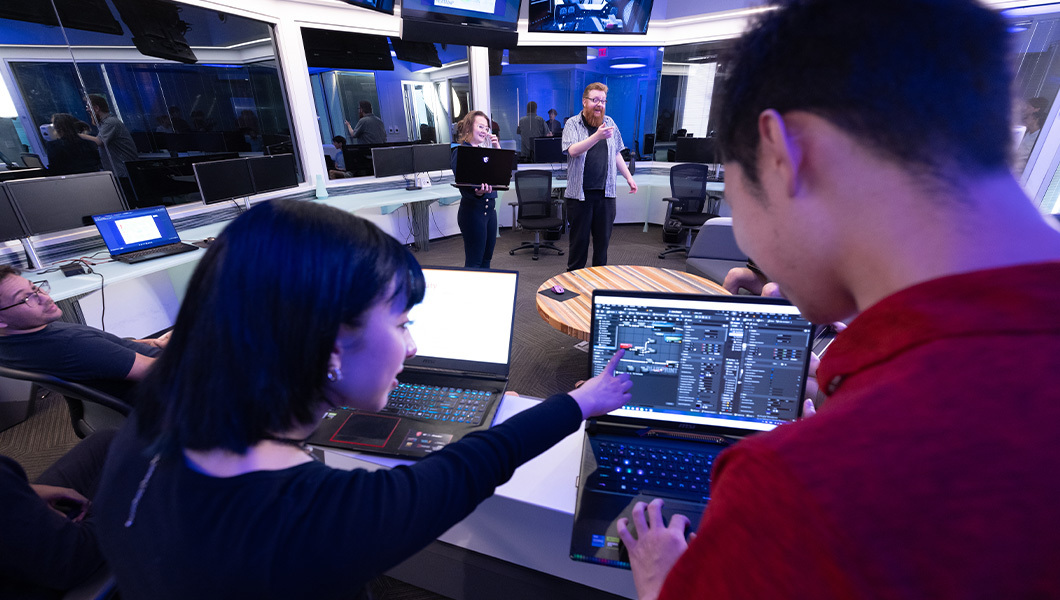 Students collaborate in the UX Lab, analyzing software and UI designs on laptops and large monitors.