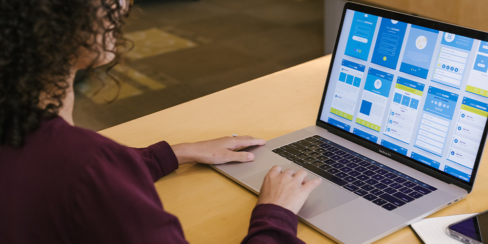 A user experience student sits at a desk and reviews mobile comps on their laptop computer.