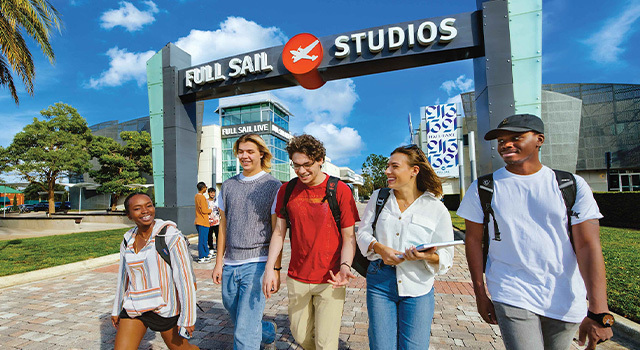 Five smiling students walk beneath the Full Sail Studios archway on a sunny day. The Full Sail Live venue is in the background.