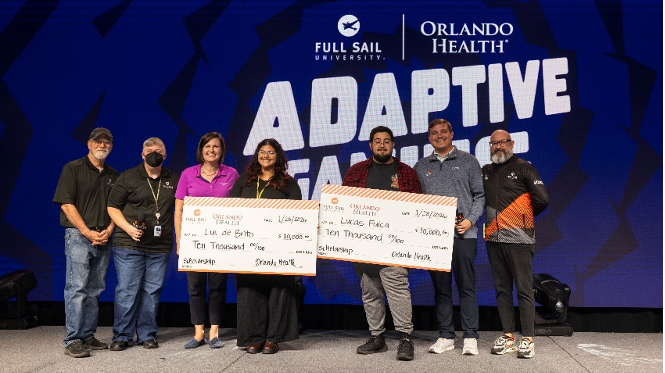 Two students hold up large checks with representatives from Orlando Health and Full Sail University.