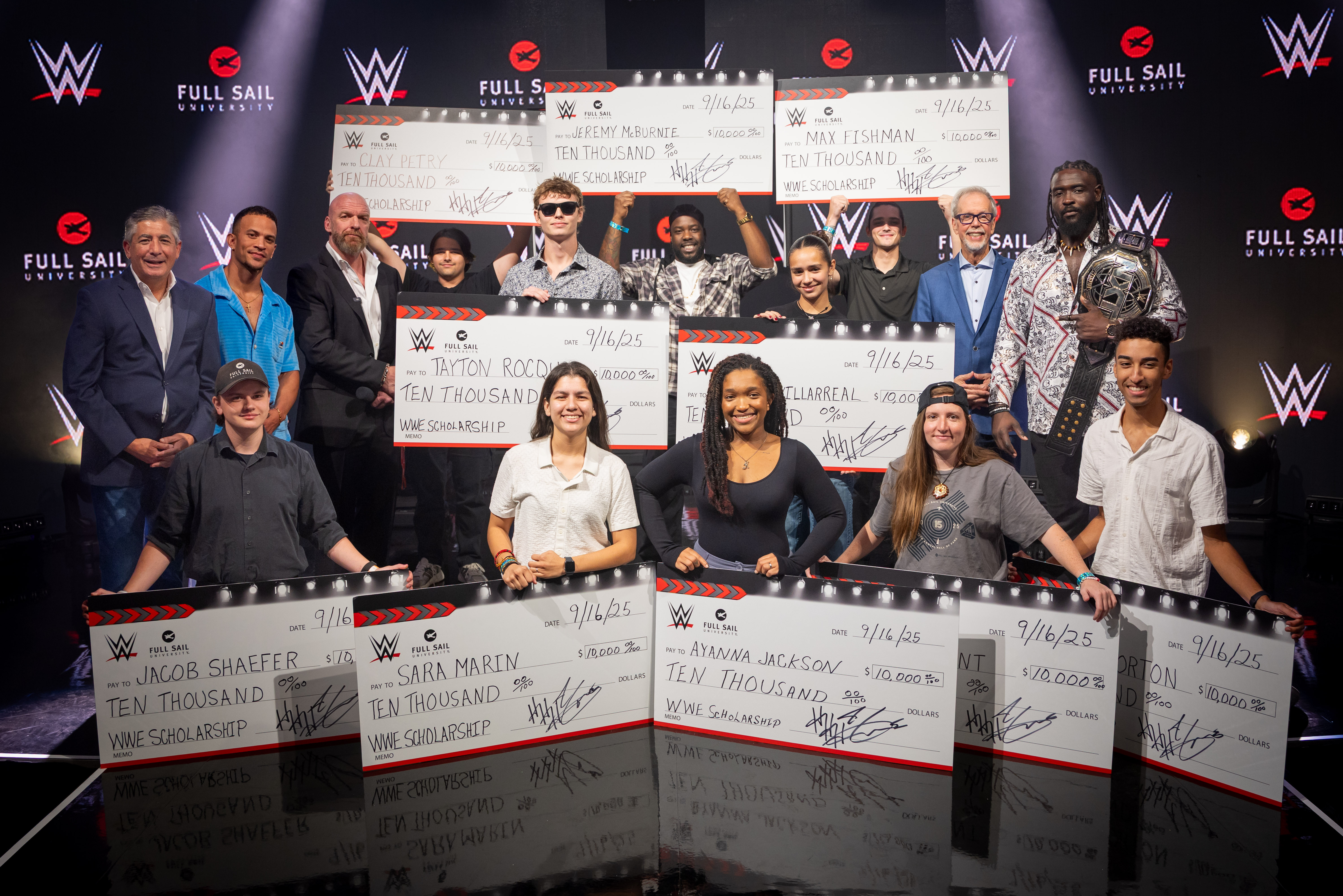 A photo with 10 Students holding up large $10,000 checks alongside WWE Stars and Full Sail President Garry Jones.