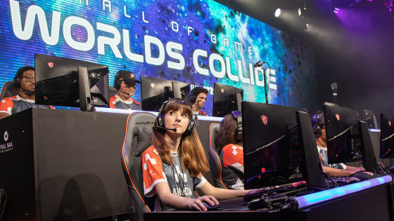 Students on Full Sail’s esports team sit at computers inside the university’s esports arena. A screen saying Hall of Game: Worlds Collide is behind them.