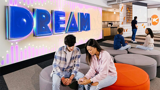 Two students sit together in front of a wall with the word Dream on it.
